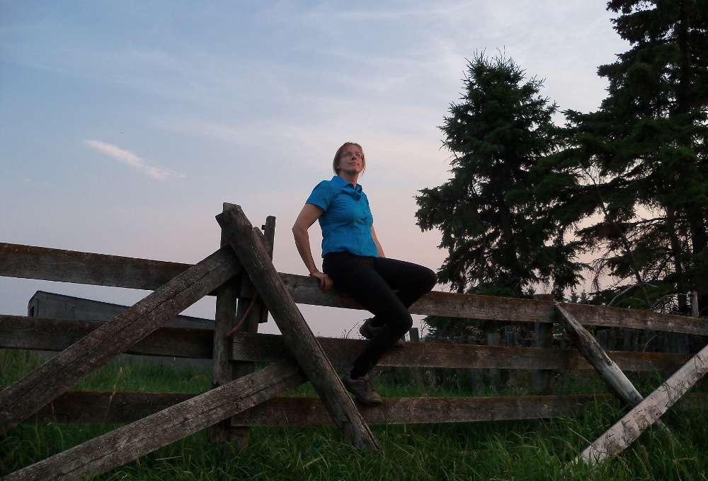 Author Teresa Griffith sitting on an old wooden fence looking contemplative.
